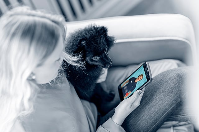 En person, der sidder på en sofa med en hund og en tablet.